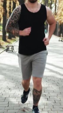 Dikey video kaslı adam koşuyor. Sporcu hızlı koşuyor. Antrenman antrenmanı dayanıklılığı zorluyor. Koşu koşucusu, parkta kulaklık takarak sıkı kardiyo egzersizi yapıyor.