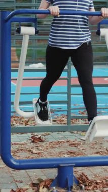 Kadının dikey format videosu dışarıda egzersiz makineleriyle çalışıyor. Sağlık için egzersiz yaparak kilo verme kavramı.