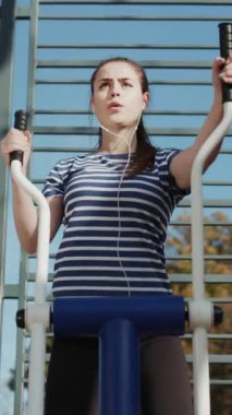 Atletizm ve spor eğitiminin dikey format videosu. Aktif yaşam tarzı ve egzersiz konsepti. Parktaki spor salonunda beden eğitimi alan bir kadın..