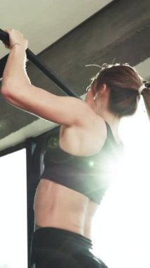 Dikey format video kaslı ince bir kızın portresi The Gyms Studio 'da çapraz çubuğu çekiyor. Kaslı, atletik kız, vücut geliştiren, kısa şortlu, simülatör çekmiş.