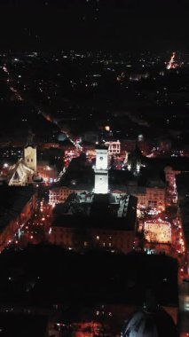 Karda Gece Şehri 'nin dikey format videosu. Gece Şehrinin Kış Panoraması. Ukrayna Lvov Şehri, Belediye Binası. Eski binaların çatıları. Noel Konsepti.