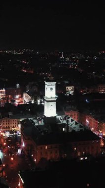 Noel süslemeleri ve ışıklarının dikey format videosu. Arial, Winter Rynok Square Caddesi 'ni vurdu. Noel Fuarı. Lvov Belediye Binası. Şehir merkezinde insanlar yürüyorlar. Gece vakti.