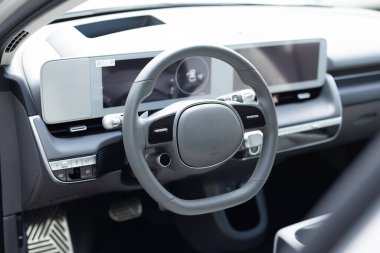 Direksiyon simidi olan pahalı bir elektrikli araba. Beyaz deri gösterge paneli, klima kontrolü, hız göstergesi, vitrin, ahşap süsleme. Araba direksiyonu..