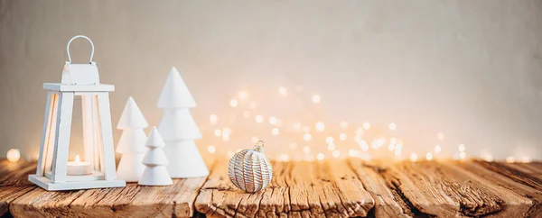 Beyaz Noel ağaçları, mum feneri ve ahşap masa üzerindeki bokeh ışıkları rahat atmosferde..