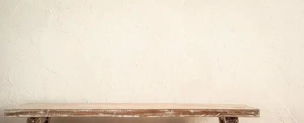 Basit bir ahşap bank dokulu bej bir duvarın önünde duruyor, ek elementler için geniş bir alana sahip minimalist bir estetiği somutlaştırıyor..