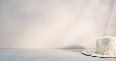 Düz bir yüzeye beyaz bir hasır şapka yerleştirilir, yaz ve rahatlama hissi uyandırır, hafif bir ışık ve gölge oyunuyla vurgulanır..