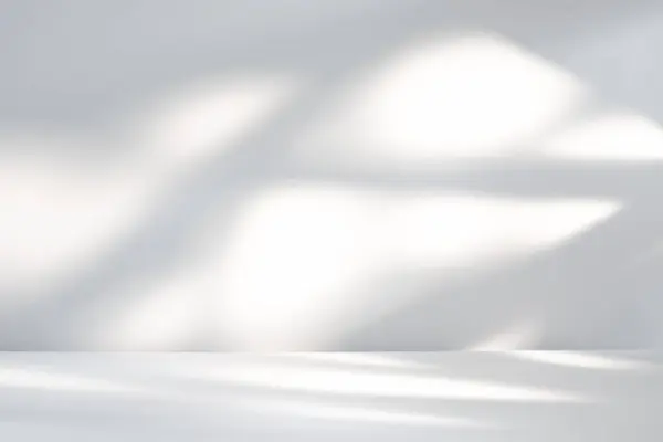 Parlak güneş ışığı, temiz beyaz bir yüzey üzerinde kapalı bir arka planda soyut gölgeler oluşturarak filtreler..