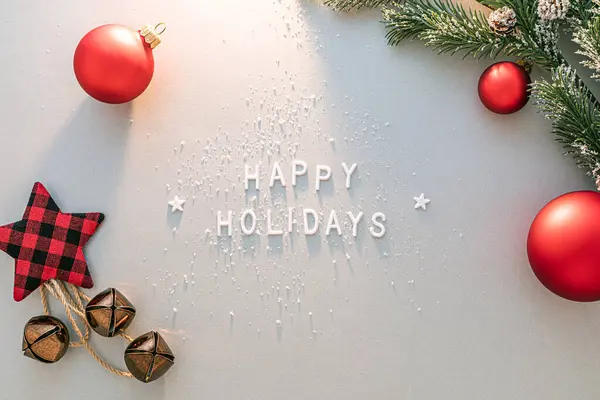 Kırmızı süslemeler, ekose yıldız, çanlar ve çam dallarıyla çevrili Mutlu Tatiller 'i anlatan beyaz harfler..