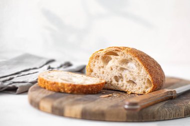 Bir somun rustik zanaatkar ciabatta, ahşap bir kesme tahtasının üzerinde dilimlenir, sabah ışığında temiz ve parlak bir mutfakta yıkanır..