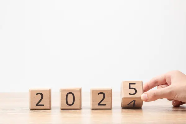 Bir el, 2024 'ten 2025' e kadar yeni yılın yaklaştığını sembolize eden ahşap bir masa üzerinde bloğu değiştiriyor..