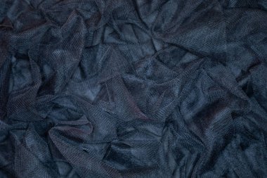 Koyu renkli bir kumaş, zengin dokularını ve ince desenlerini ortaya çıkararak bir yüzey boyunca uzanır. Gölgelerin ve gölgelerin etkileşimi ilgi çekici bir görsel etki yaratır..