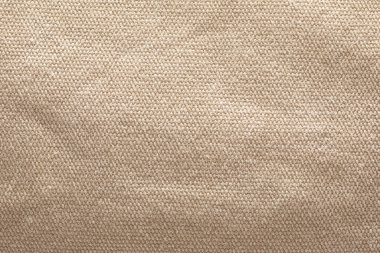 Fotoğraf, kaba bej kumaşın detaylı bir yakın çekimini, ince ışıkla vurgulanmış karmaşık dokusunu ve dokuma kalıplarını gözler önüne serer..