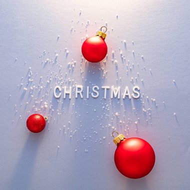 Parlak kırmızı Noel süsleri, Noel 'i anlatan beyaz harflerin etrafına sanatsal bir şekilde yerleştirilmiş, yumuşak bir zemine saçılmış kar ile tamamlanmış..