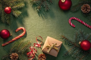 Kırmızı Noel süsleri, çizgili şeker kamışları ve yeşil dallar ve çam kozalaklarıyla çevrili bir hediye kutusu neşeli bir tatil atmosferi yaratır..