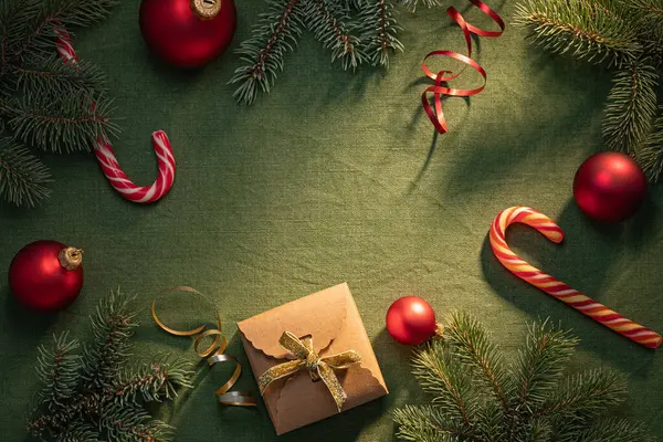 Altın kurdeleli kahverengi hediye kutusu, kırmızı süslemeler, şeker kamışları ve yeşil kumaş arkaplanda ebedi yeşil dallar, Noel ve kış tatilleri için mükemmel..