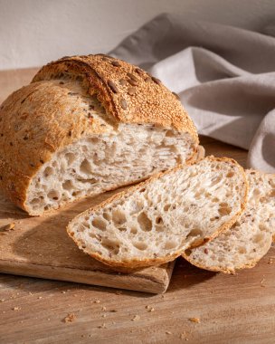 Tahta kesme tahtasının üzerinde taze pişmiş tam tahıllı ekmek ve yanında dilimler..