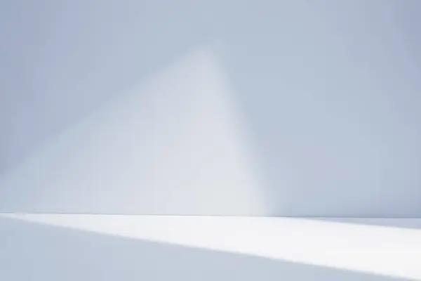 Parlak güneş ışınları, sabah erken saatlerde yumuşak gölgelerle donatılmış minimalist beyaz bir oda arkaplanı aydınlatıyor..