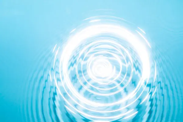 Dairesel dalgalanmalar berrak mavi sularda, parlak ışık altında sakin bir yerde yayılıyor..