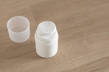 Silinebilen kapağı olan beyaz krem konteynır pürüzsüz bir ahşap yüzeyde duruyor. Günışığı, kullanılabilirliğini ve modern estetiği vurgulayarak, parlak tasarımını vurguluyor..