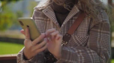 Parkta telefon kullanan bir kadın. Elinde cep telefonu olan kıvırcık saçlı bir kız. Elinde akıllı telefon tutan bir kadın. Yüksek kalite 4k görüntü