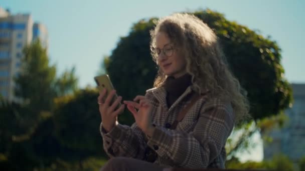 Γυναίκα Που Χρησιμοποιεί Τηλέφωνο Κάθεται Στο Πάρκο Curly Κορίτσι Γυαλιά — Αρχείο Βίντεο