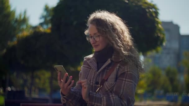 Женщина Телефоном Сидит Парке Кудрявая Девушка Очках Держит Мобильный Телефон — стоковое видео