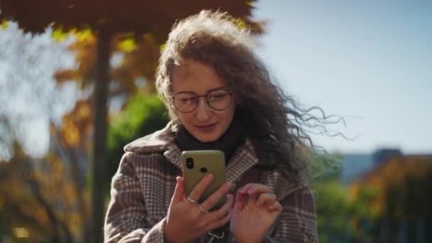 Mujer Sorprendida Usando Teléfono Sentado Parque Chica Rizada Con Gafas — Vídeos de Stock
