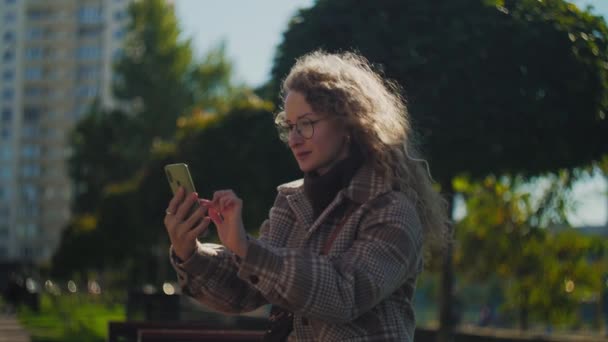 Donna Sorpresa Utilizzando Telefono Seduto Nel Parco Ragazza Riccia Con — Video Stock