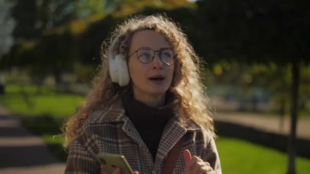 Γυναίκα Ακούστε Μουσική Ακουστικά Στο Πάρκο Curly Κορίτσι Απολαμβάνοντας Χρήση — Αρχείο Βίντεο