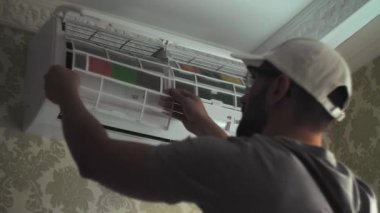 Odanın duvarındaki beyaz klima ünitesine odaklanmış genç tamirci temiz filtreler. Gri iş kıyafetleri tamiri uzmanı. Yüksek kalite 4k görüntü