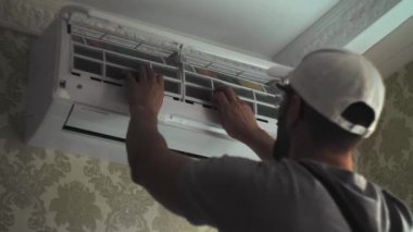 Odanın duvarındaki beyaz klima ünitesine odaklanmış genç tamirci temiz filtreler. Gri iş kıyafetleri tamiri uzmanı. Yüksek kalite 4k görüntü