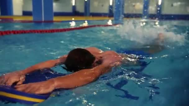 水泳インストラクターは若い男にプールで泳ぐ方法を教えています インストラクターの監督の下で屋内プールで泳ぐスポーツと健康的なライフスタイル 高品質のフルHd映像 — ストック動画
