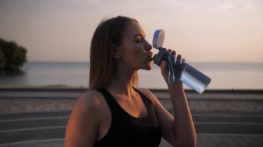 Spor salonunda su içen fitness kızı. Oyun sahasında denizin önünde duran kız. Antrenmandan sonra su iç. Yüksek kalite 4k görüntü