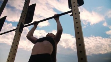 Barlarda barfiks çeken atletik bir kız. Dışarıda egzersiz yapan bir kadın. Gökyüzüne karşı sokak çalışması. Yüksek kalite 4k görüntü