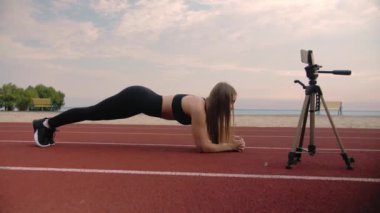 Tahtada duran fitness kızı. Oyun parkında akıllı telefonla ders veren bir kadın. Sahilde dışarıda antrenman yapıyor. Yüksek kalite 4k görüntü