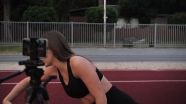 Fitness kız blogcusu sicimde oturuyor ve internette telefon kullanarak ders veriyor. Kumsalın önünde uzaktan çalışıyor. Gün batımı. Yakın çekim. Yüksek kalite 4k görüntü