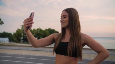 Genç fitness kızı telefonla selfie çekiyor. Bayan arkadaşlarıyla bir video görüşmesi yapıyor. Güzel bir deniz ve plajın önünde duran bir kadın. Yüksek kalite 4k görüntü