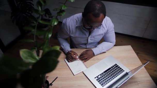 自宅でオンライン学習を行うアフリカの男性 ビジネス人は ノートPcを使用してリモートで動作します ノートパッドに書いて黒人男性のトップビューは コンピュータ上で遠隔教育を行います 高品質4K映像 — ストック動画
