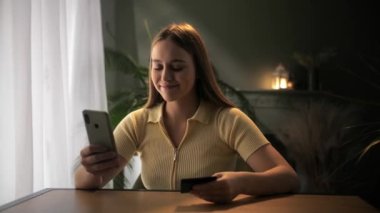 Kadın kredi kartı bilgilerini akıllı telefondan giriyor. Banka işlemleri yapan genç bir kız. Masada oturan ve cep telefonuyla kart bilgilerini satın alan bir kadın. Yüksek kalite 4k