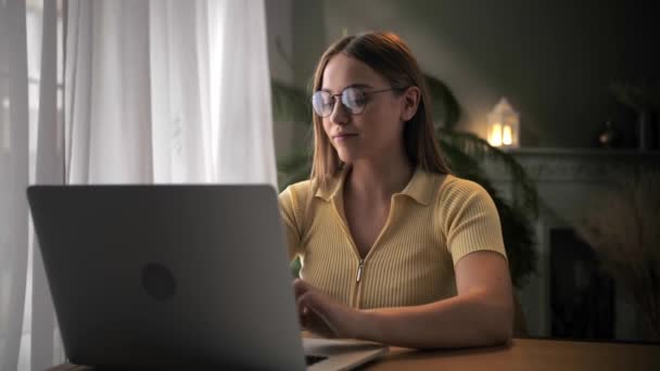 女人坐在家里的桌子边 用笔记本电脑远程工作 年轻的金发姑娘在键盘电脑上打字 在家里学习在线课程 — 图库视频影像
