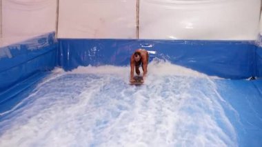 İçerideki dalga simülatöründe sörf yapan çekici adam. Genç sörfçü, üretilmiş dalgalar üzerine eğitim alırken. Su sporu aktivitesi. Sörfçü adam sörf taklitçisi olarak sörf yapmayı seviyor. Sörf eğitimi