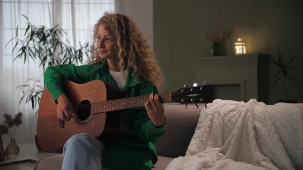 Kvinna Spelar Akustisk Gitarr Sittandes Soffan Heminredning Ung Lockig Tjej — Stockvideo