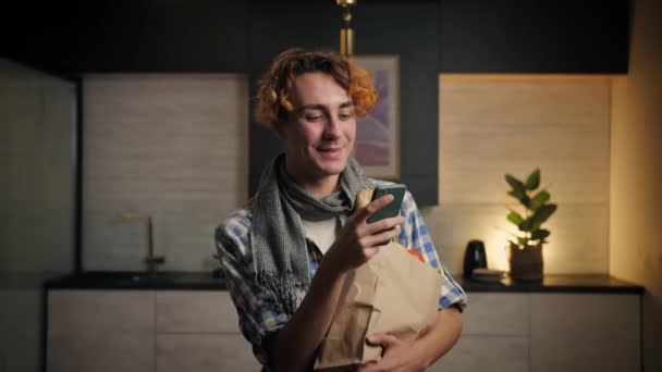 Joven Hombre Pie Con Bolsa Comestibles Usando Teléfono Kitchen Checking — Vídeos de Stock