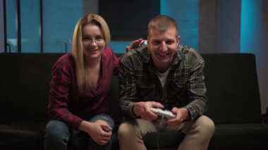 Sevgilisi oturma odasında ona destek olurken video oyunu oynayan bir adam. Genç adam konsol ekranı kullanarak TV seyrediyor. Evdeki kanepede oturup eğleniyor. Kumar bağımlılığı. Yüksek kalite 4k