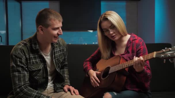 女人在家里教男人怎么弹吉他 夫妻坐在沙发上学习乐器 男人和女人学习音乐家的业余生活方式 高质量的4K镜头 — 图库视频影像