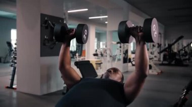 Siyah adam spor salonunda egzersiz yaparken bençe uzanıyor ve halterli ağırlık kaldırarak egzersiz yapıyor. Vücut geliştirme konsepti. Yüksek kalite 4k