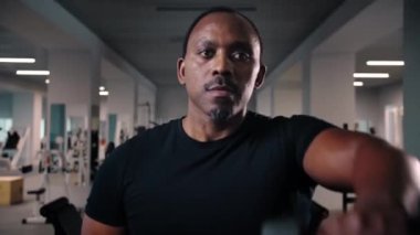 Spor salonunda halterli antreman yapan siyah bir adam. Kas geliştiren, kas çalıştıran, dambıl tutan, ağır dambıllar tutan, Afrika kökenli Amerikalı ağırlık kaldıran bir adam. Yüksek kalite 4k