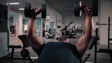 Siyah adam spor salonunda egzersiz yaparken bençe uzanıyor ve halterli ağırlık kaldırarak egzersiz yapıyor. Vücut geliştirme konsepti. Yüksek kalite 4k