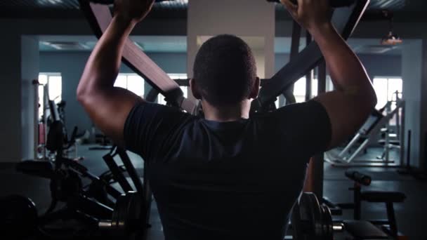 训练背部肌肉的黑人男子在健身房做举重运动 运动员在模拟器新设备中做运动 健美运动员坐在健身房的机器上 高质量的4K镜头 — 图库视频影像