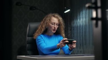 Genç Kıvırcık Kadın akıllı telefonuyla evde oturmuş video oyunu oynuyor. Cep telefonu tutan genç kızın portresi evde oyun oynamaktan zevk alıyor. Gençlik yaşam tarzı ve teknoloji konsepti. Yüksek kalite 4k görüntü